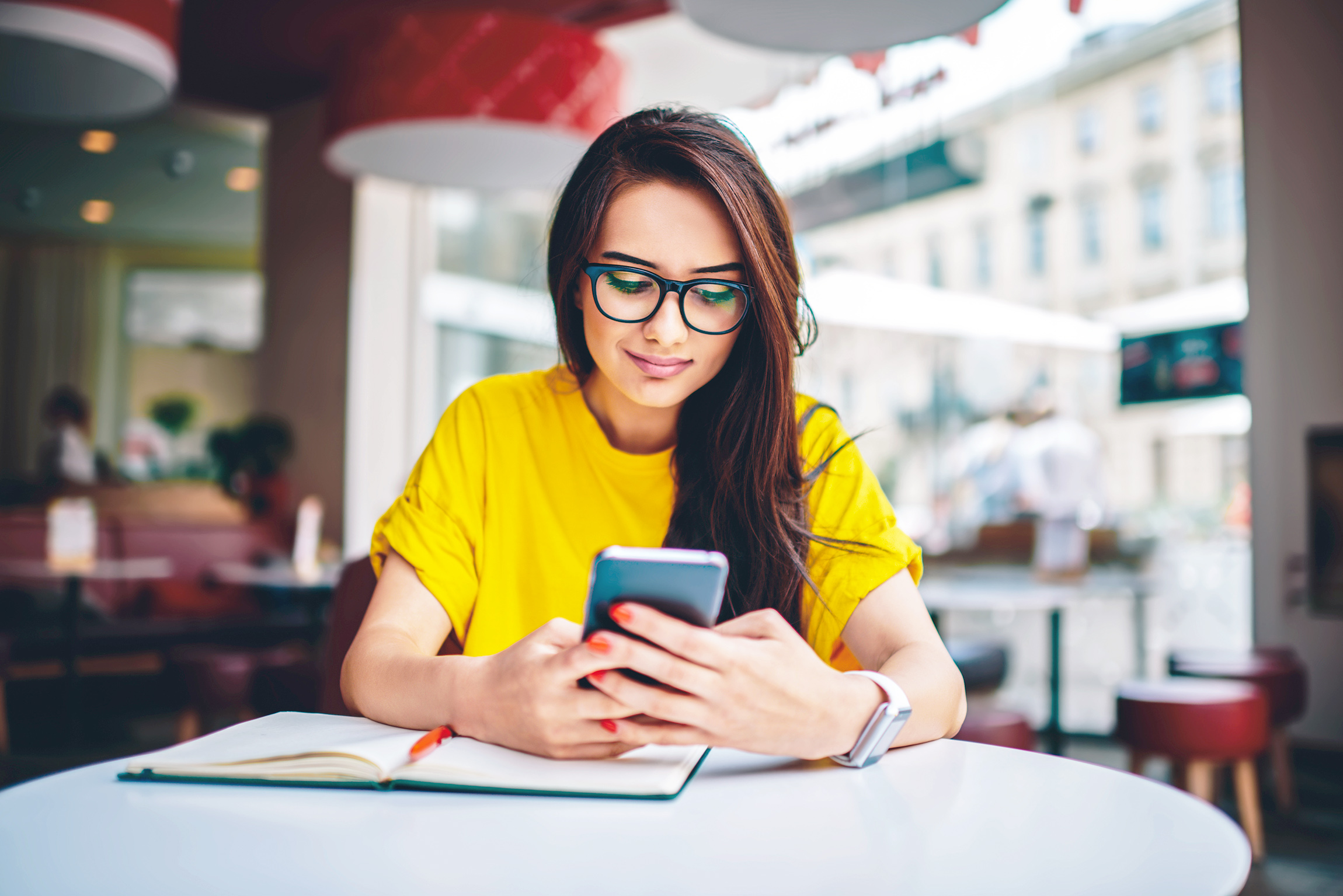 A woman looking at her phone in a cafe, with a book on the table.