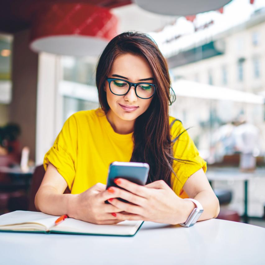 A woman looking at her phone in a cafe, with a book on the table.